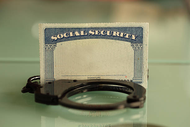 A blank Social Security card standing upright between a set of handcuffs on a glass surface.