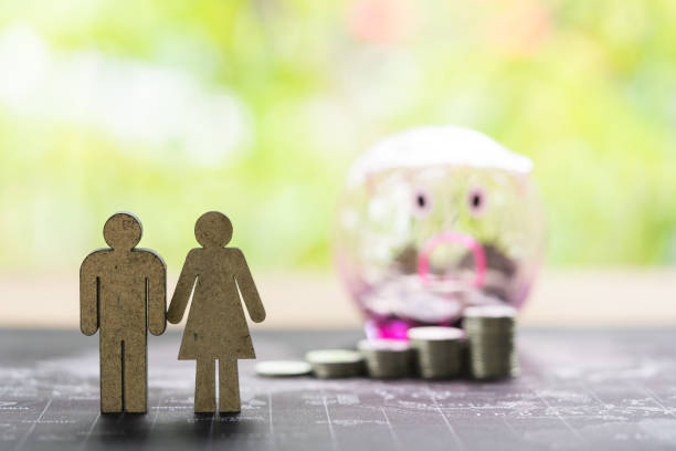 Wooden man and woman figurines standing in front of coin stacks and a piggy bank.